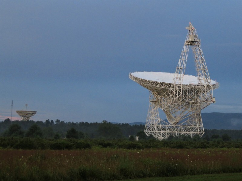 Green Bank Telescope at dusk: a giant white off-axis dish atop a lattice tower, dwarfing a smaller dish telescope in the distance