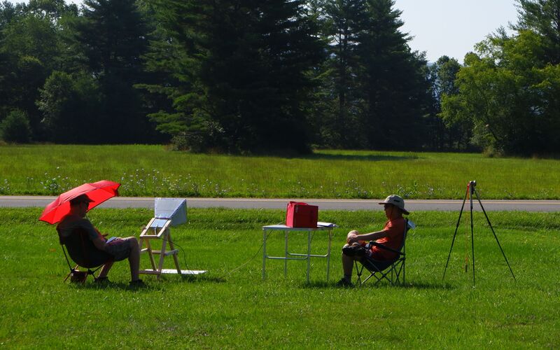 Two observers running a horn telescope from camp chairs in a field.