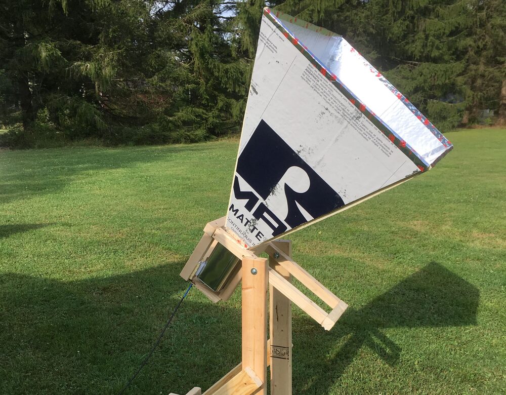 A finished horn telescope standing in a field. The pyramidal antenna is folded from foil-faced insulation board and feeds a square paint-thinner can at its throat; below it, a wooden cradle lets the horn turn in elevation on a stand of dimensional lumber.