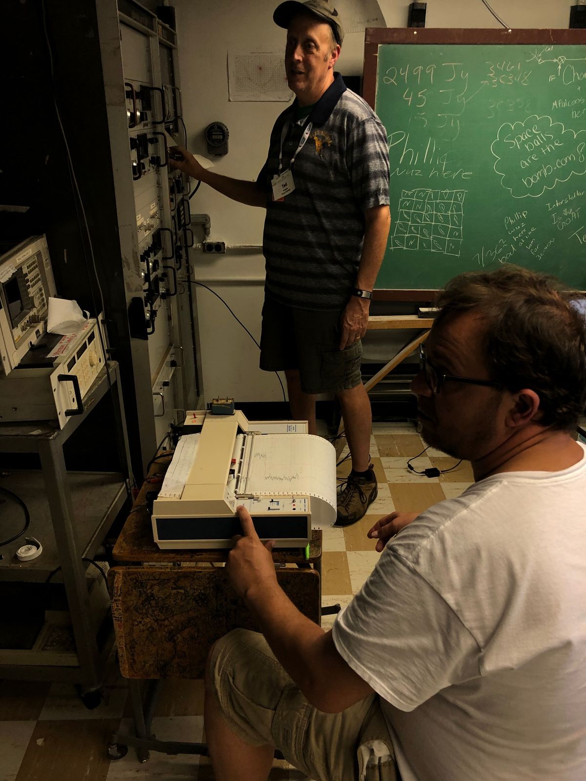 Teachers at work in an equipment room at the Green Bank Observatory, one of them writing at a chalkboard