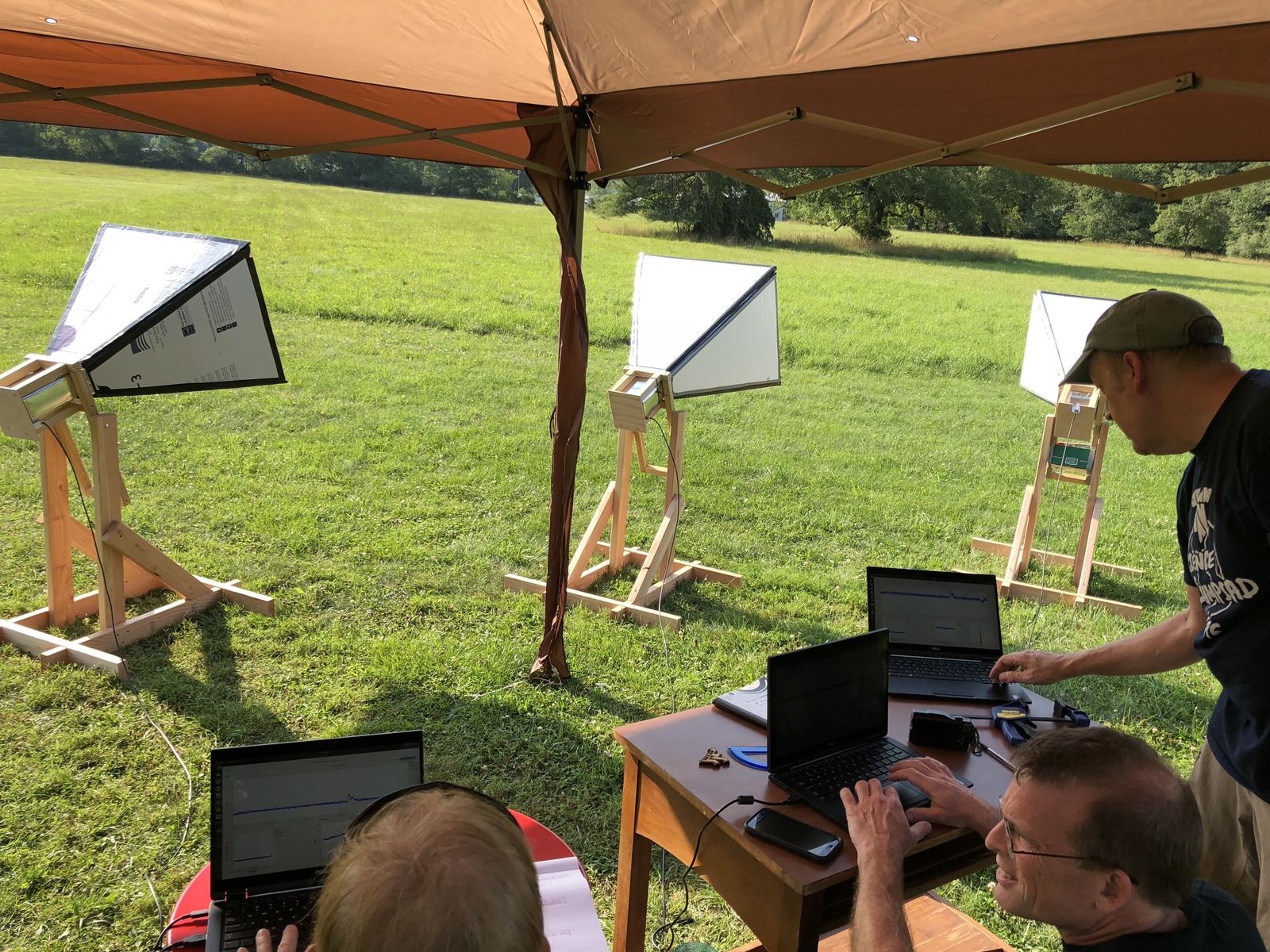 Three horn antennas on wooden mounts under a canopy on the lawn at Green Bank, with teachers at laptops beside them