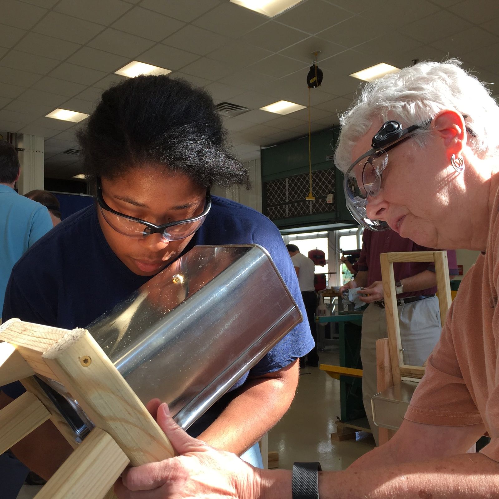 Two teachers working a metal cylinder into shape at a bench in the WVU workshop