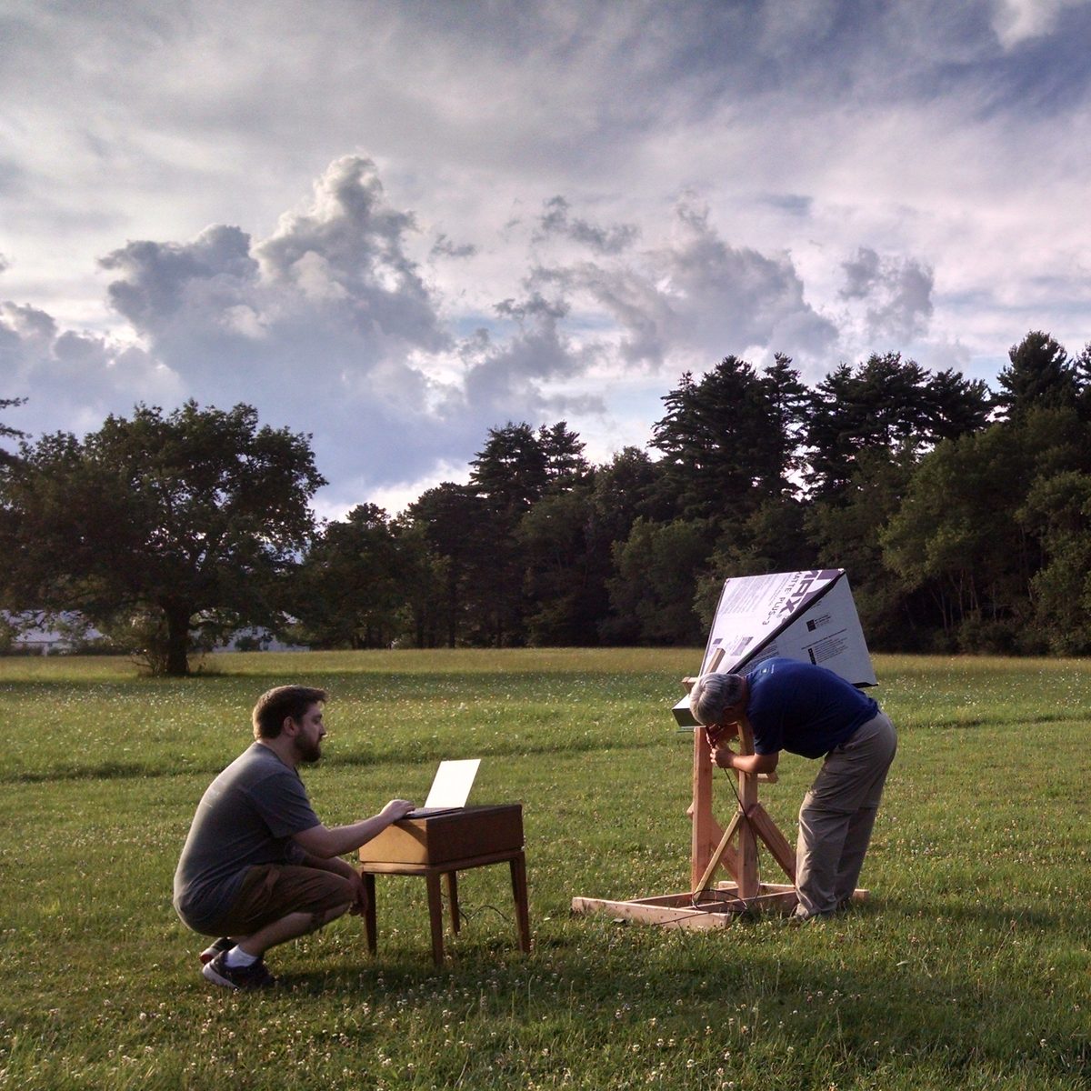 Two DSPIRA teachers operating a small horn radio telescope in a field at dusk